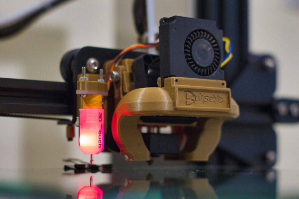 Detailed shot of a 3D printer nozzle operating in a workshop setting.